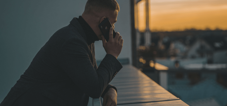 man using mobile phone on balcony at sunset