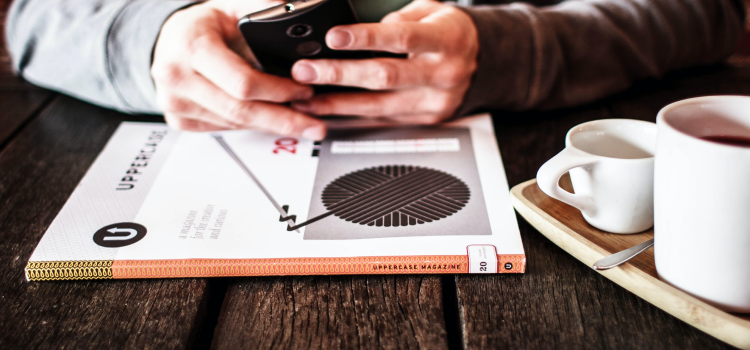 person using phone at table with book and coffee